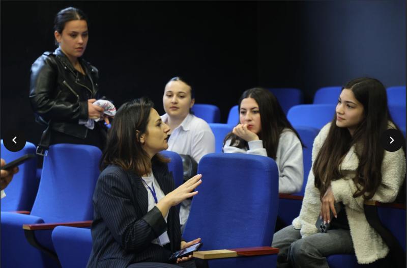 A teacher sat in a auditorium with four female students, engaged in talking to them