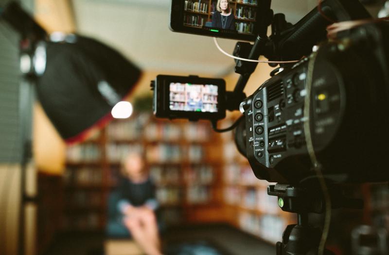 image of a video camera setup in a room, focused on a female at the front of the room, who is blurred out