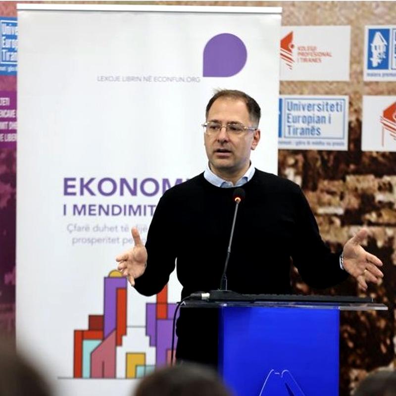 A male workshop speaker stood at a lectern at the front of a hall, speaking to a group of people that we cannot see