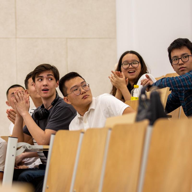 Students sat in a lecture hall, focused on something happening behind them which makes them smile
