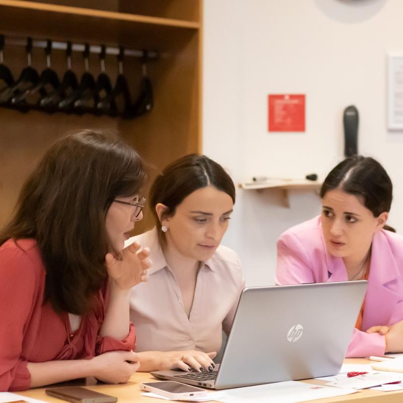 Three females working together at a desk and looking at one shared laptop screen