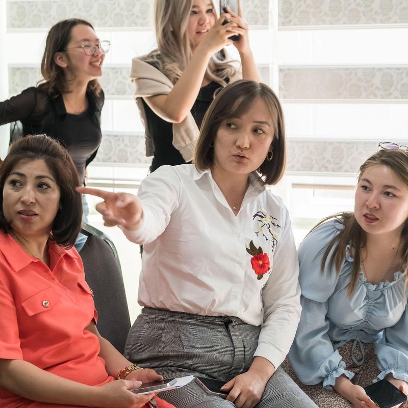 A group of several female adults, with one pointing to the left, and all looking in the same direction