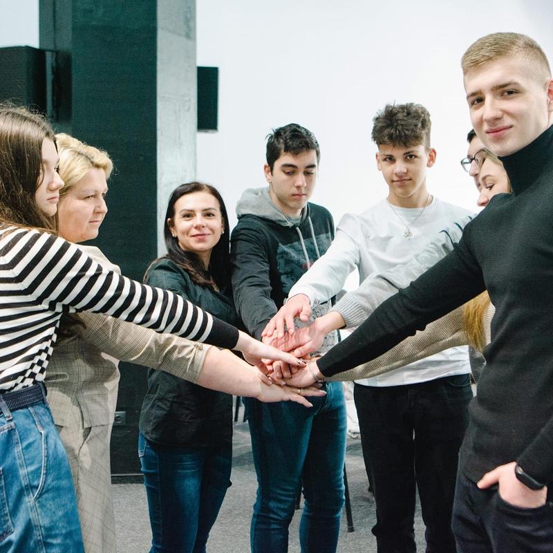 Group of students in a circle placing one hand on top of each others in the middle
