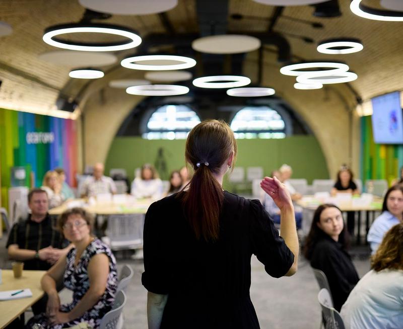 Looking at the back of a teacher trainer, who is facing forward and speaking to engaged adults